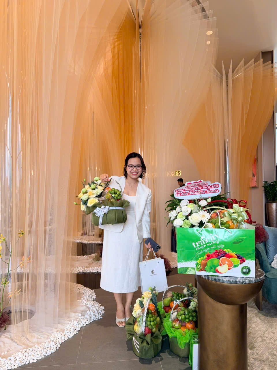 Đàm Lương mặc trang phục trắng, cầm giỏ hoa tại sảnh dự án